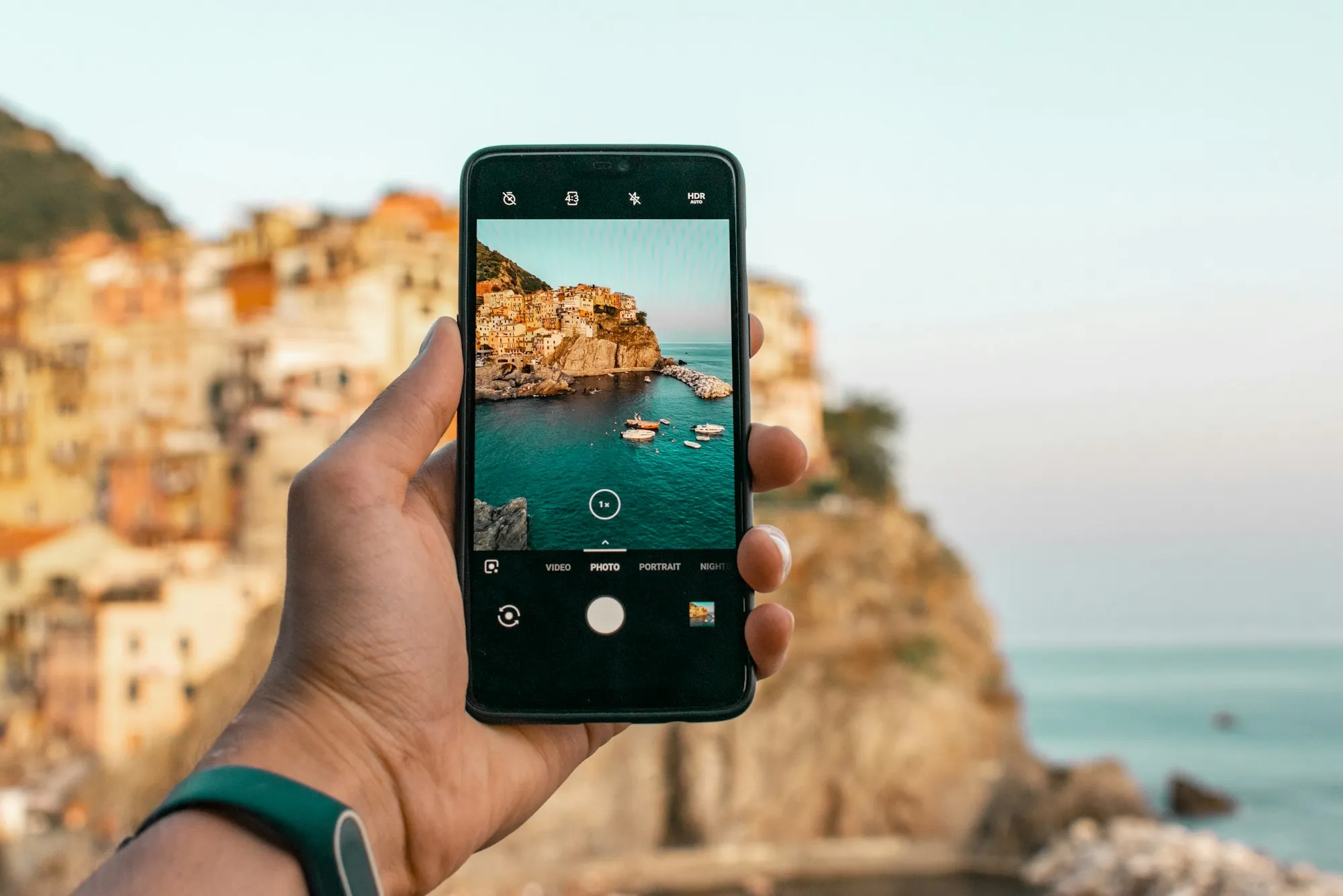 Hand filmt mit dem Smartphone eine Küstenstadt am Meer